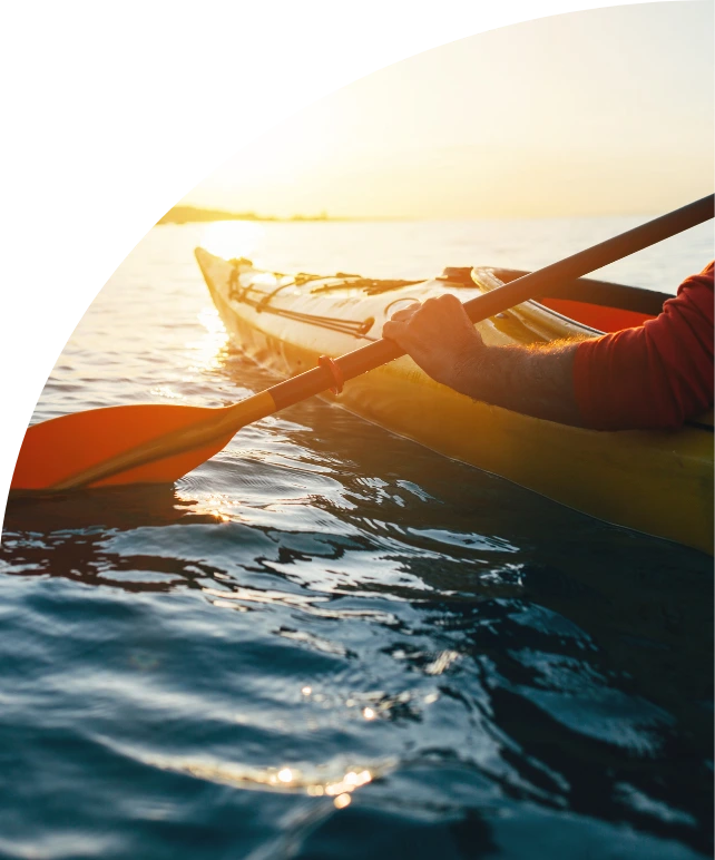 Kayak sur un lac au soleil couchant, la pagaie levée au-dessus de l'eau