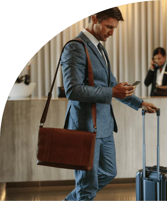 A business traveller with a suitcase checks his phone as he crosses the lobby, in front of the front desk